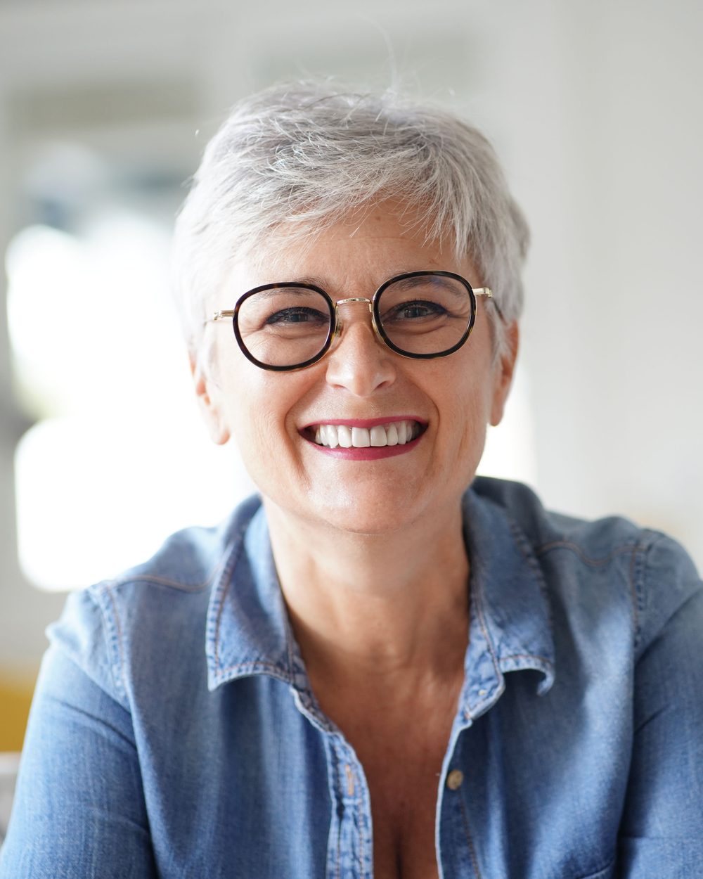 A smiling woman with short dark hair going grey and round glasses