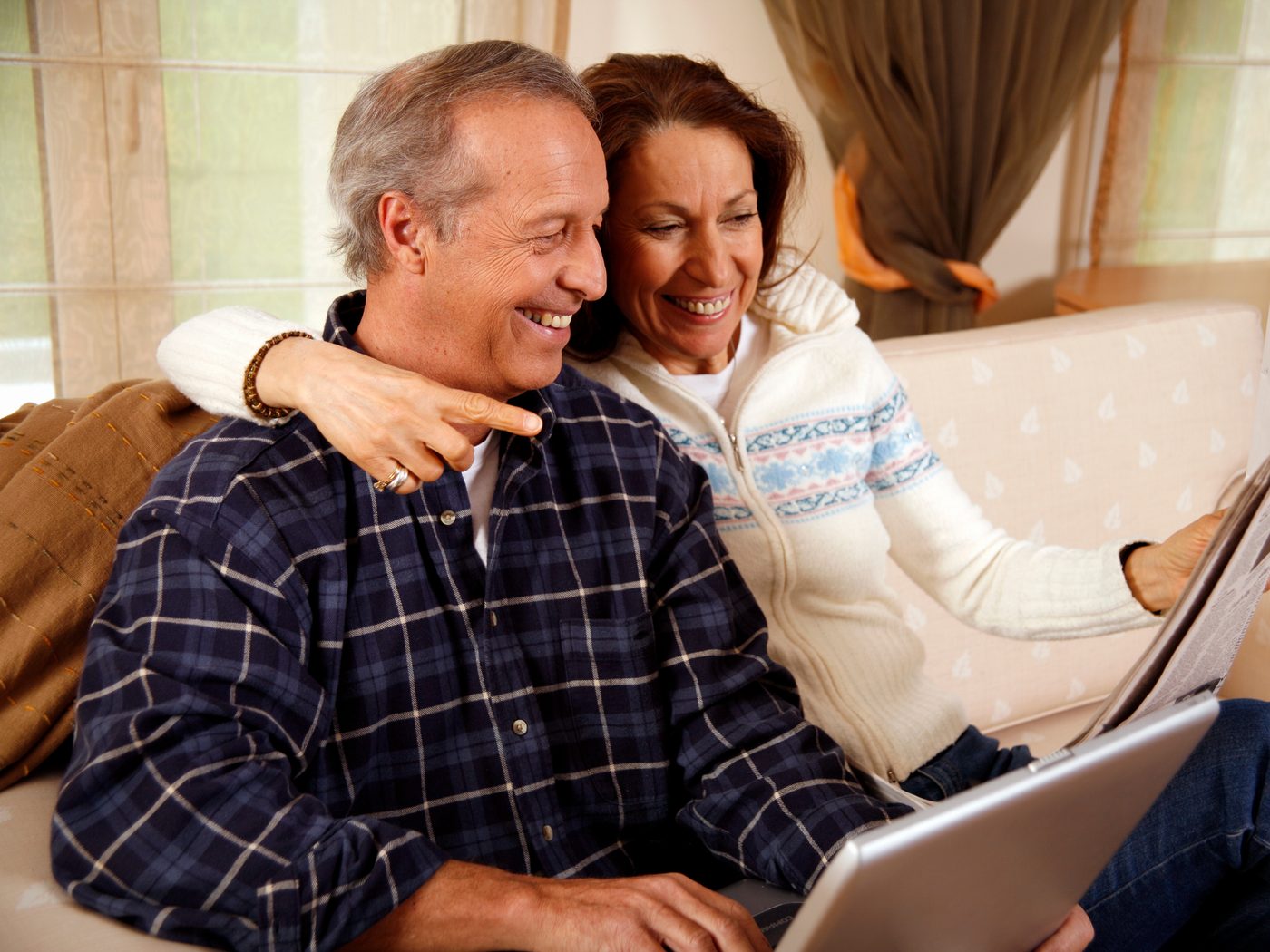 A couple laughing on the couch while reading the paper together