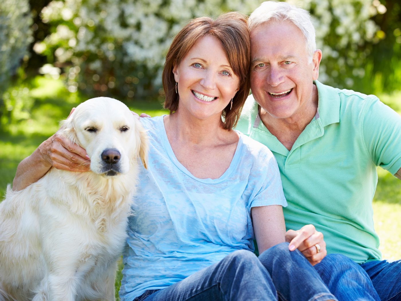 A couple sitting on the grass with their golden retriever