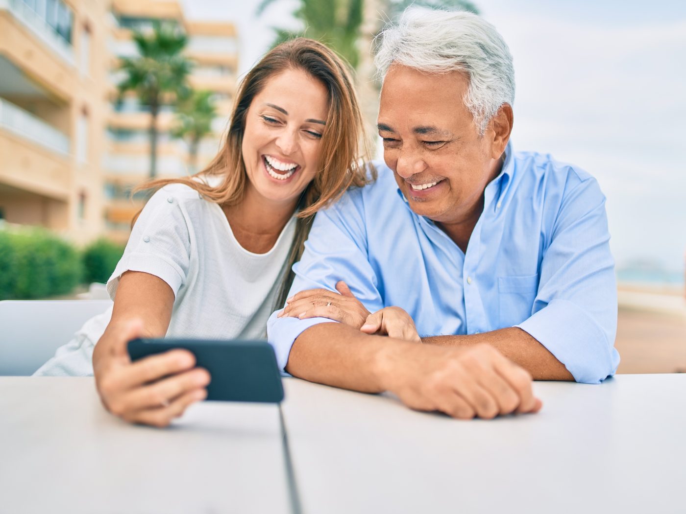 A couple leaning in together to look at a phone at an outdoor table