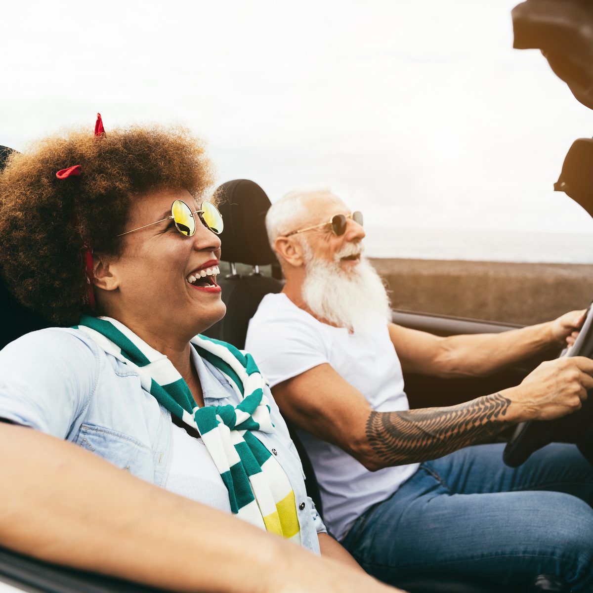 A couple laughing in a convertible on a sunny road trip