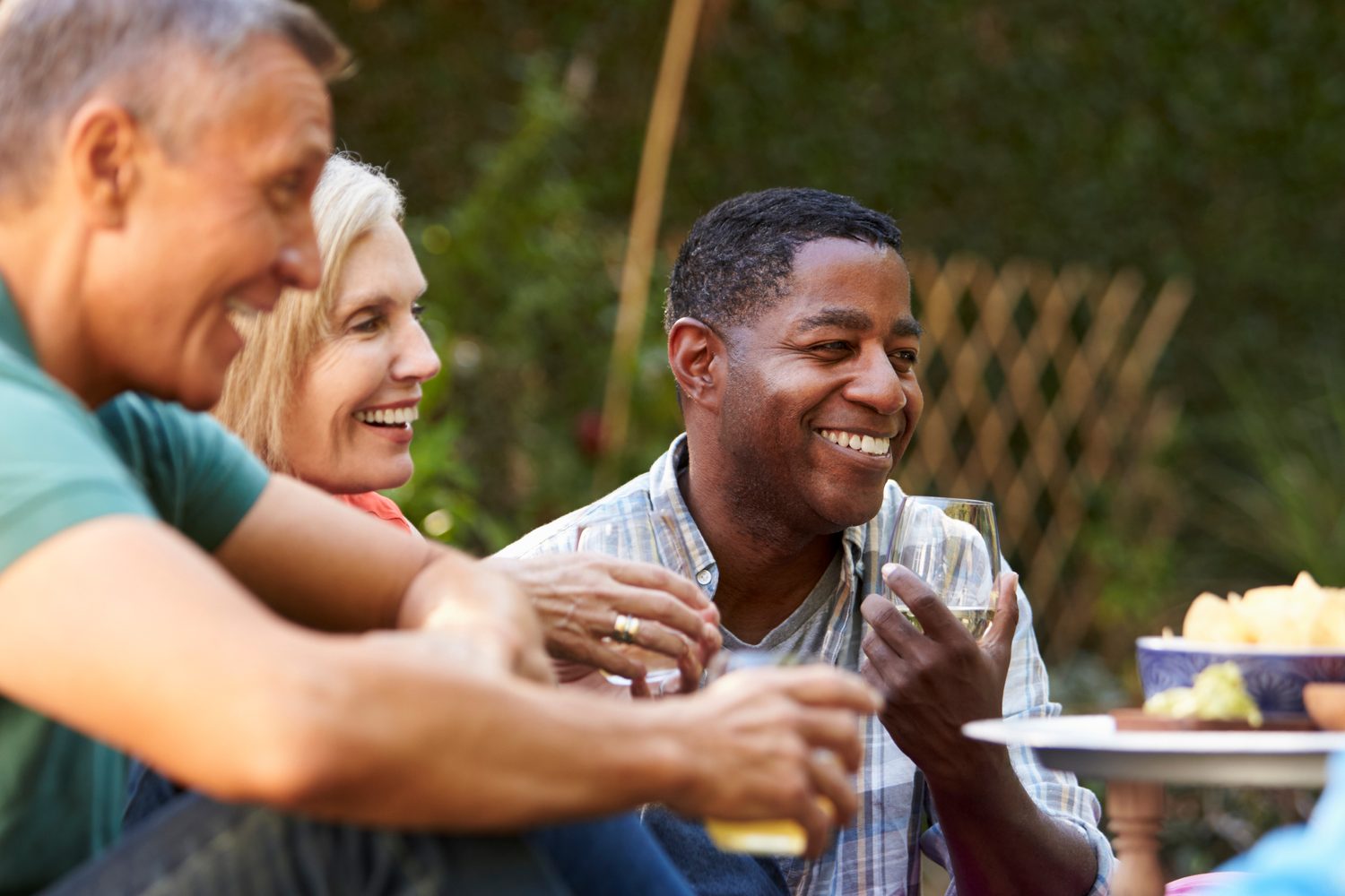 Three friends laughing together over drinks at a backyard get-together