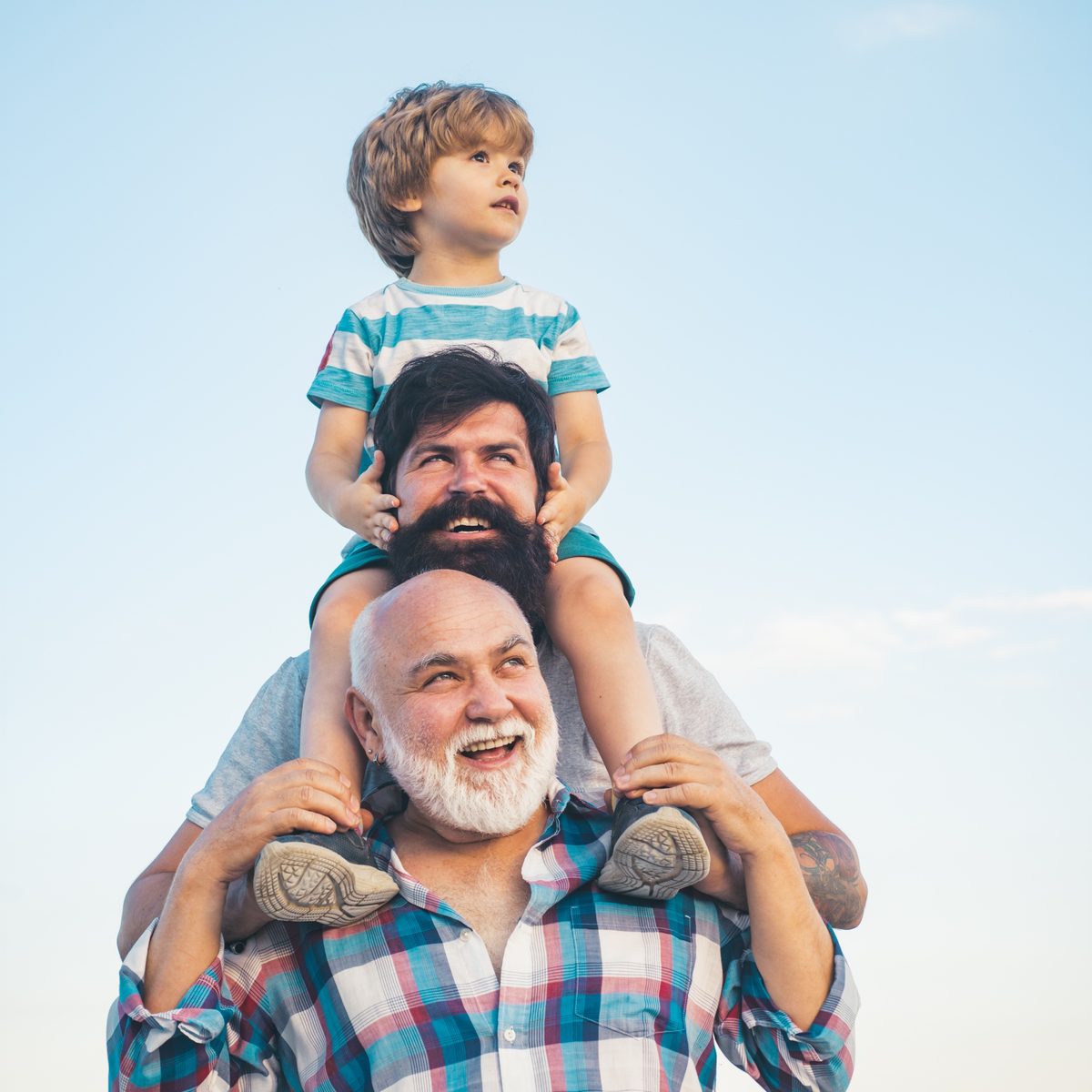 Three generations: a grandfather with his grown son on his shoulders, and a grandson on top